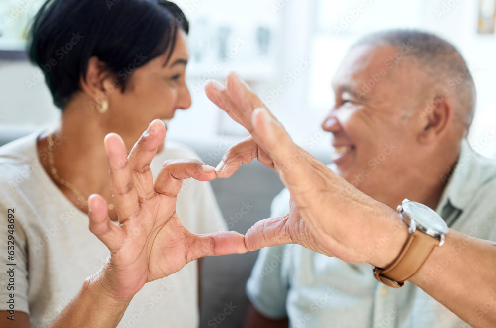 Heart shape, hands and senior couple bonding and talking in the living room of their home. Happy, sm