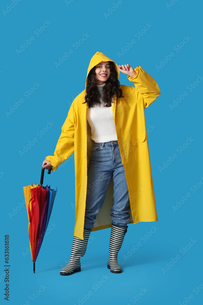 Teenage girl in raincoat with umbrella on blue background