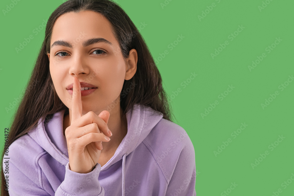 Beautiful young woman showing silence gesture on green background, closeup