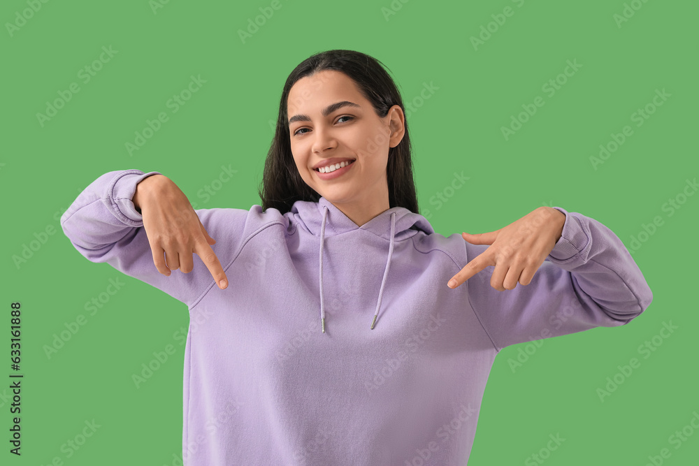 Beautiful young woman pointing at her hoodie on green background