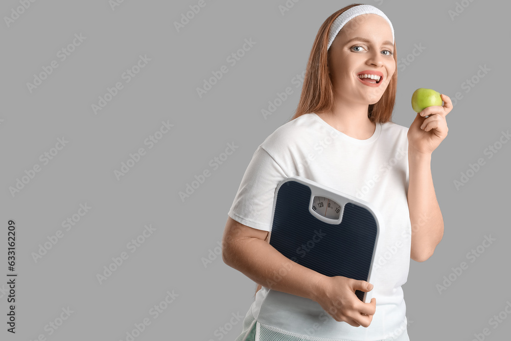 Young overweight woman with scales and apple on grey background