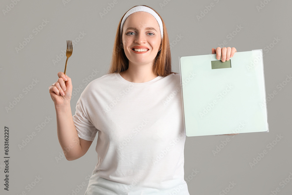 Young overweight woman with scales and fork on grey background