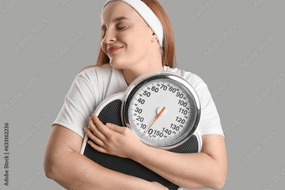 Young overweight woman with scales on grey background, closeup