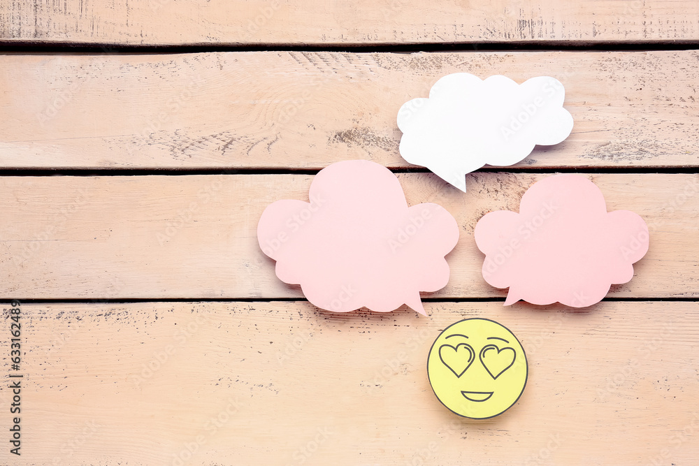 Paper face with heart eyes and blank speech bubbles on beige wooden background