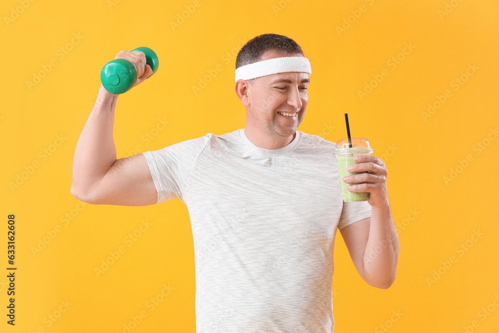 Sporty mature man with glass of vegetable smoothie and dumbbell on yellow background