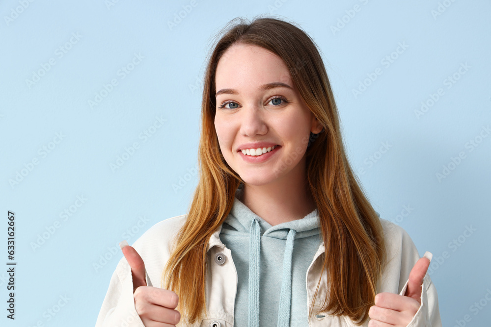 Beautiful young woman showing thumbs-up on blue background