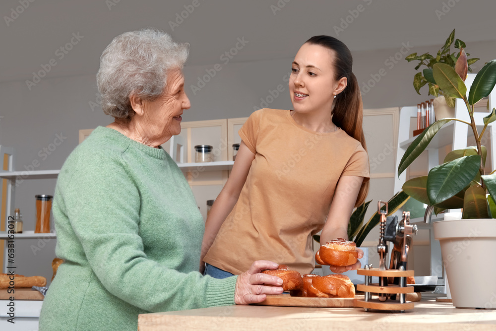 Senior woman with her granddaughter and tasty buns in kitchen