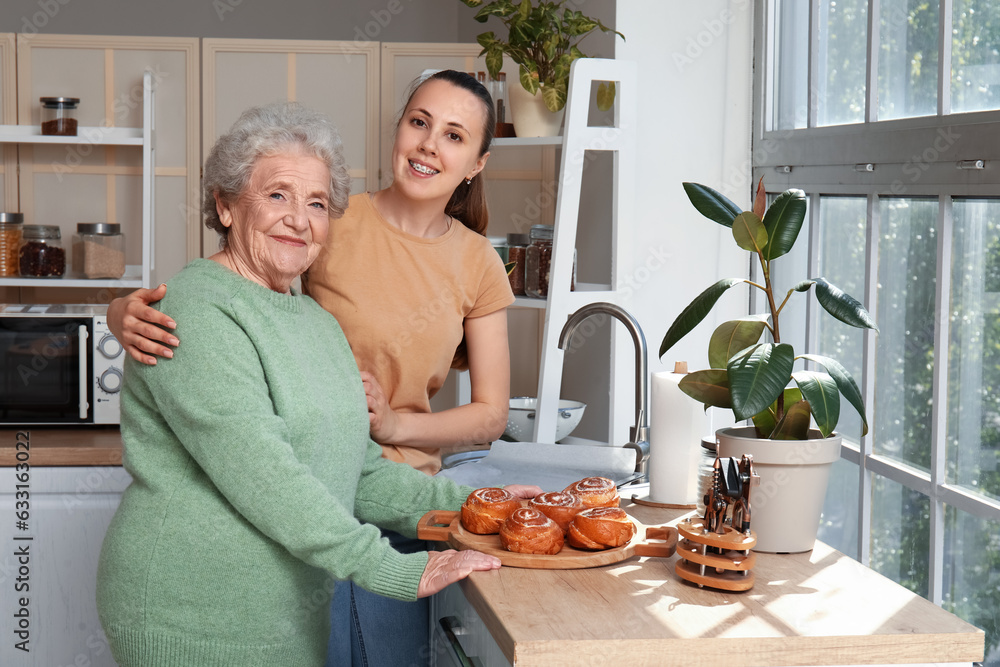 Senior woman with her granddaughter and tasty buns in kitchen