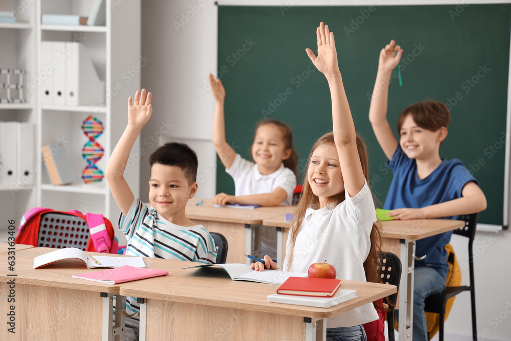 Little pupils raising hands during lesson in classroom