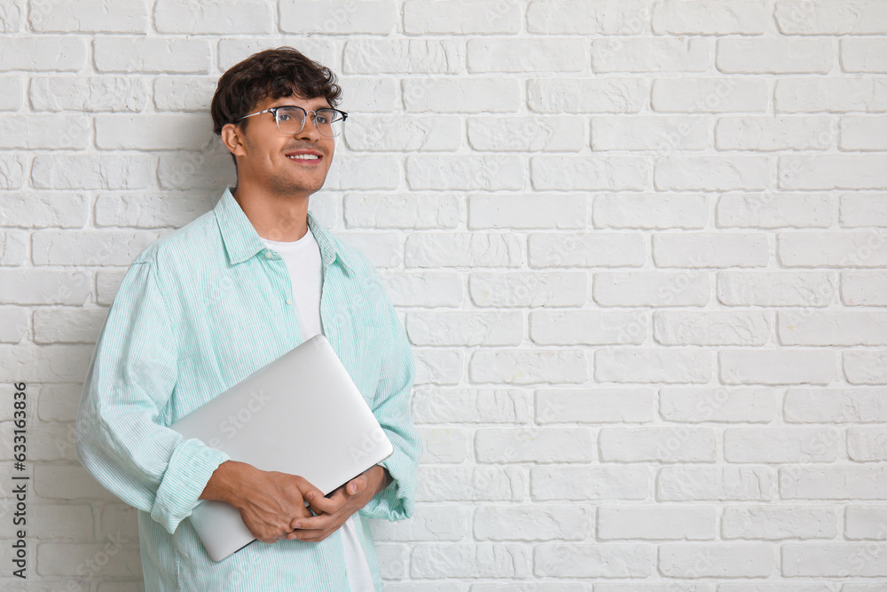 Male programmer with laptop on white brick background