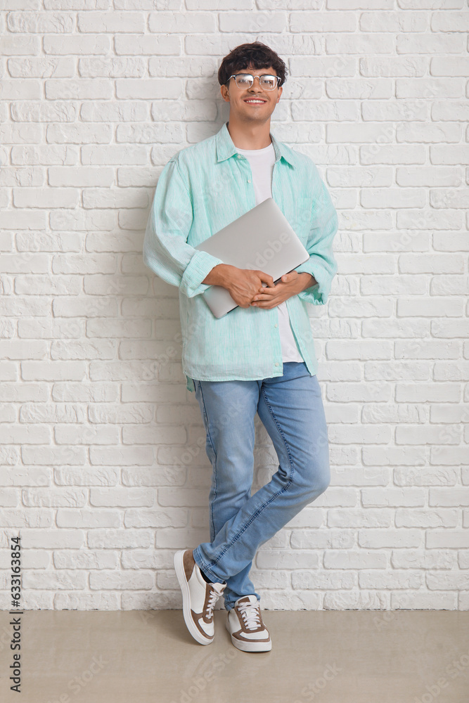 Male programmer with laptop near white brick wall