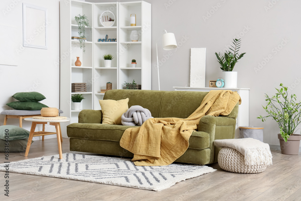 Cozy green sofa with soft blanket and cushions in interior of light living room