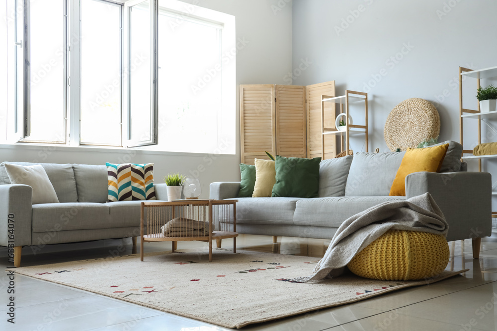 Cozy grey sofas and pouf with soft blanket in interior of light living room