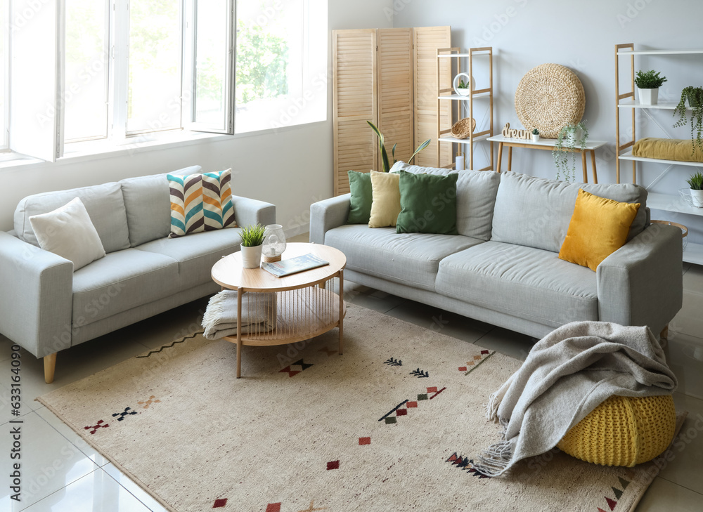 Cozy grey sofas and pouf with soft blanket in interior of light living room