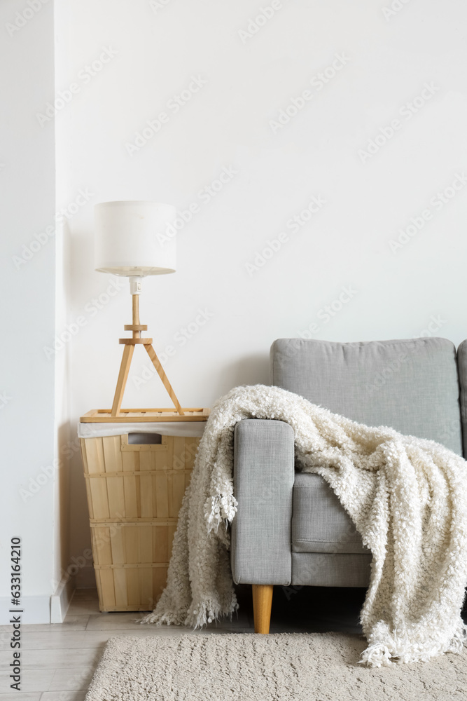 Cozy grey sofa with soft blanket in interior of light living room