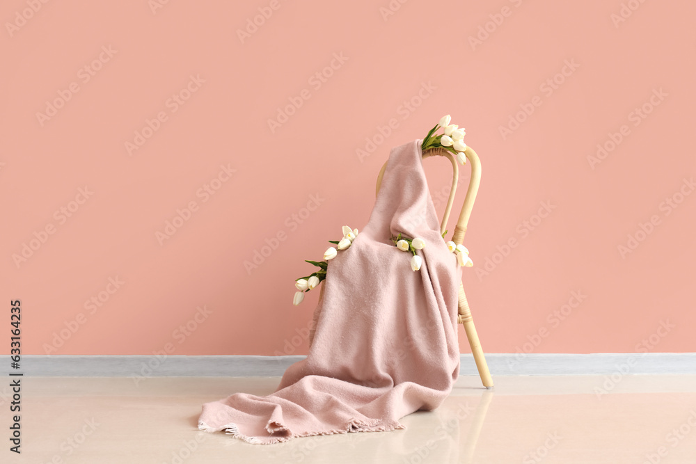 Chair with plaid and tulips near pink wall in room