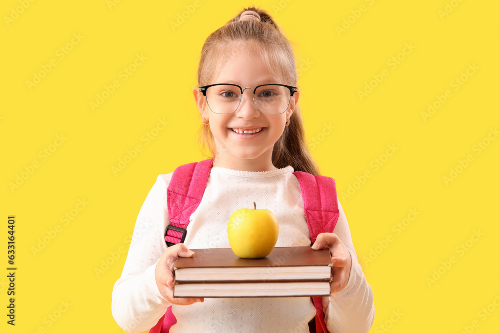 Little schoolgirl with books and apple on yellow background