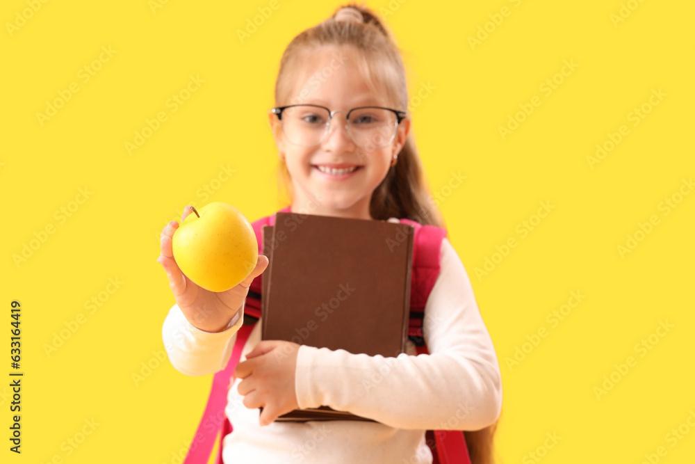 Little schoolgirl with books and apple on yellow background