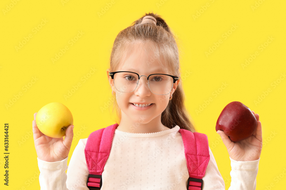 Little schoolgirl with apples on yellow background