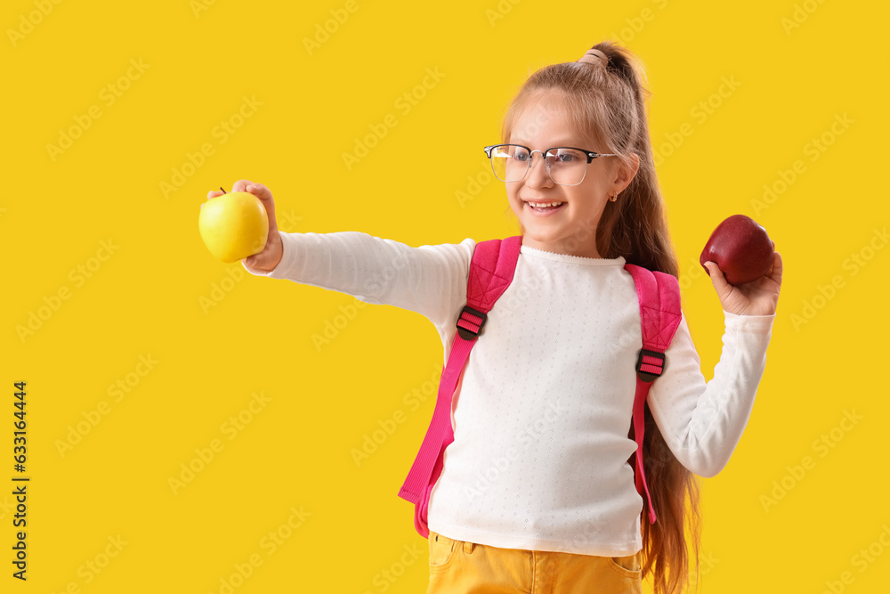 Little schoolgirl with apples on yellow background