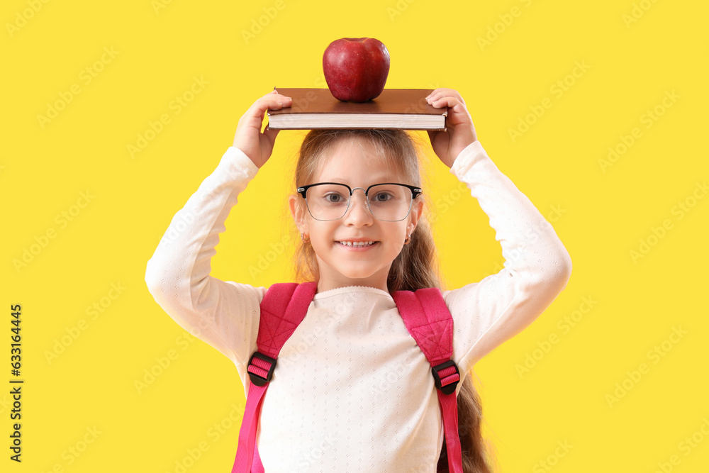 Little schoolgirl with book and apple on yellow background