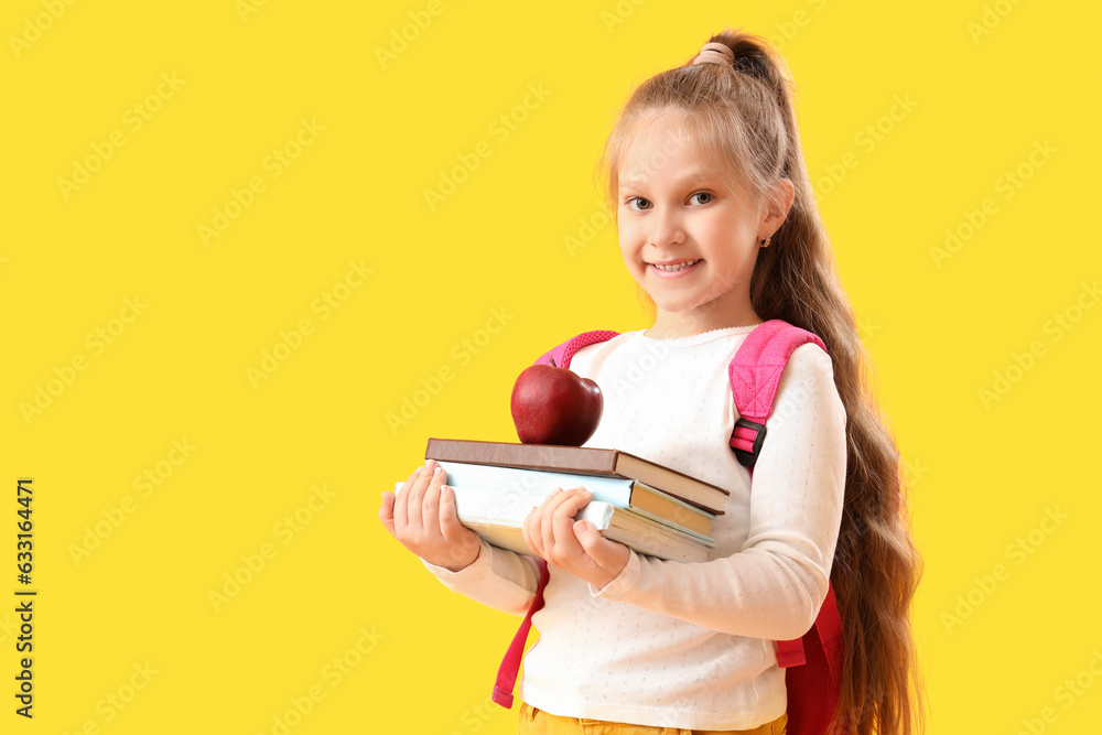 Little schoolgirl with books and apple on yellow background