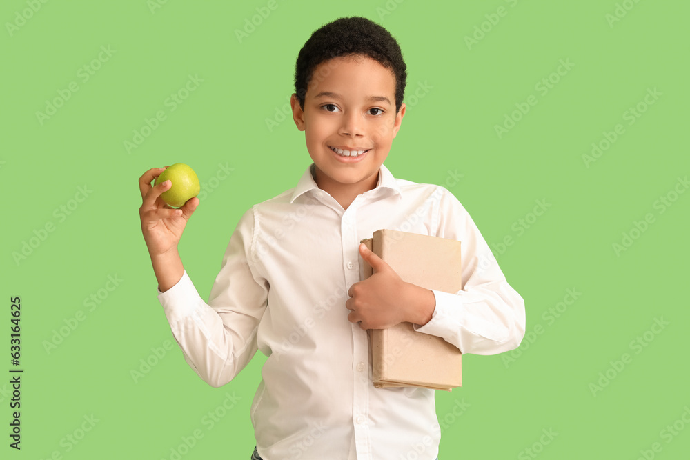 Little African-American schoolboy with books and apple on green background