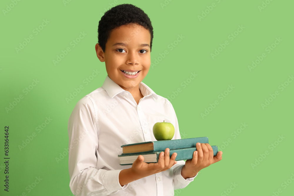 Little African-American schoolboy with books and apple on green background