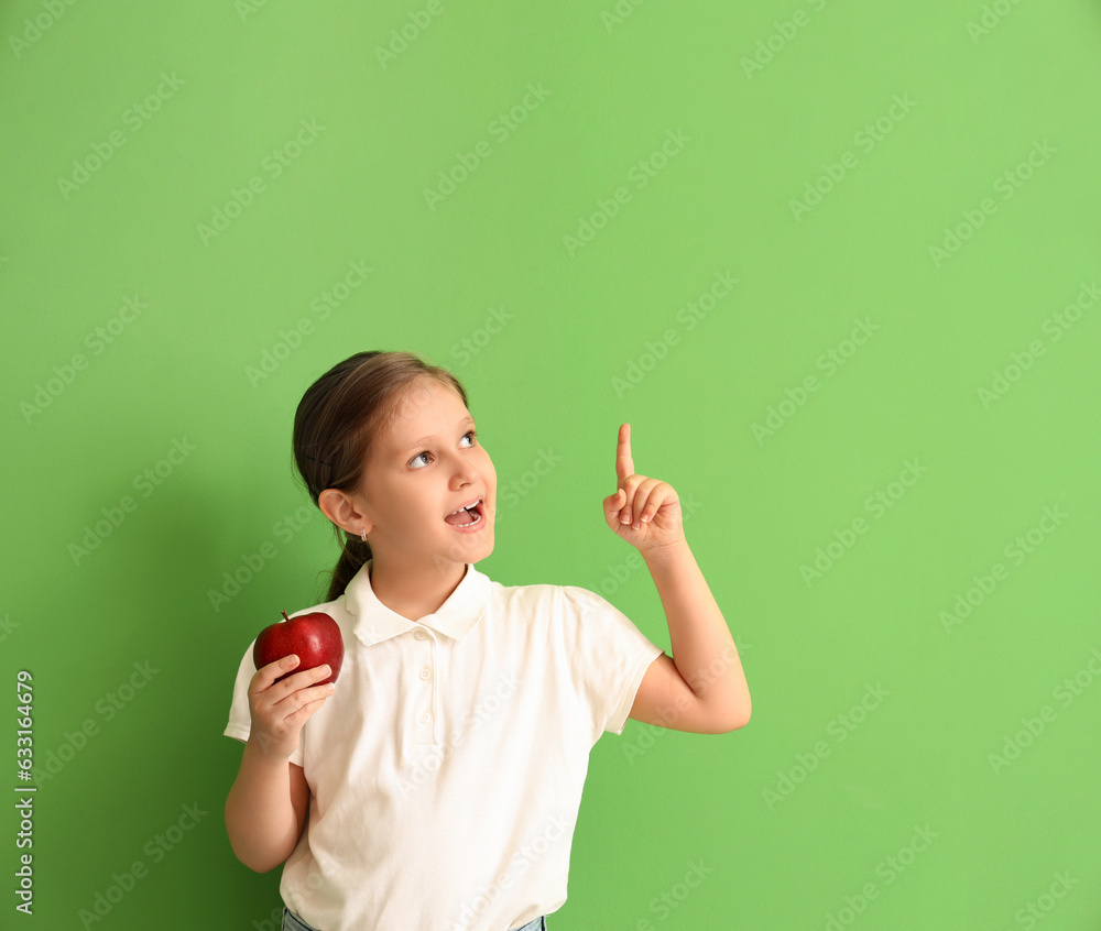 Little girl with apple pointing at something on green background