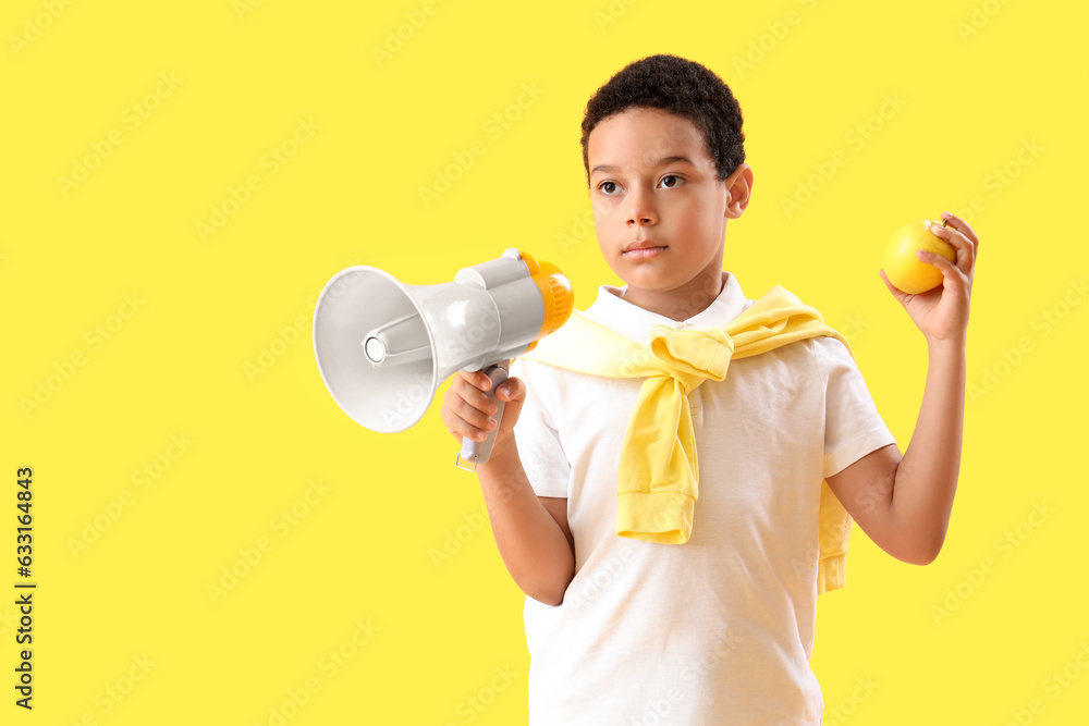 Little African-American boy with megaphone and apple on yellow background