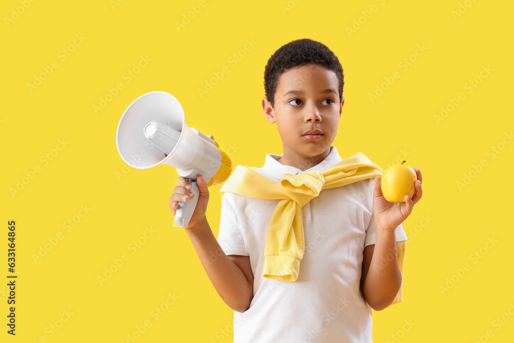 Little African-American boy with megaphone and apple on yellow background