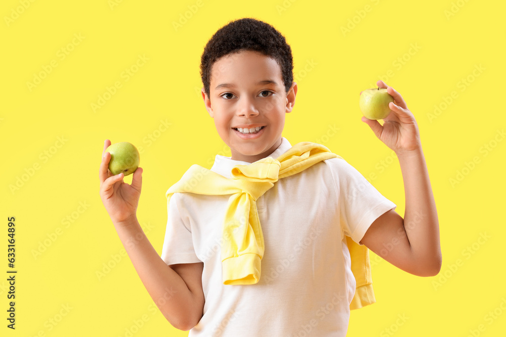 Little African-American boy with apples on yellow background