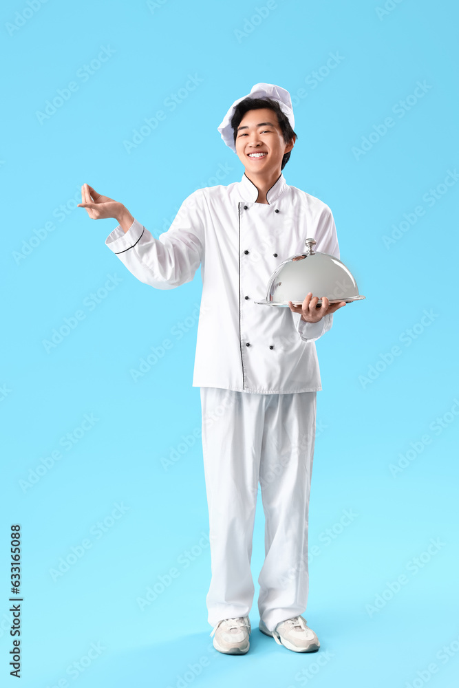 Male Asian chef with cloche gesturing on blue background