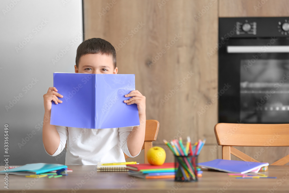 Cute little boy with copybook doing homework in kitchen