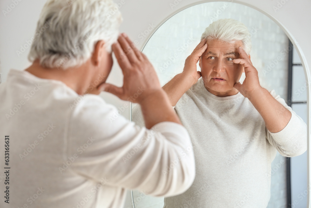 Shocked senior man looking in mirror at home