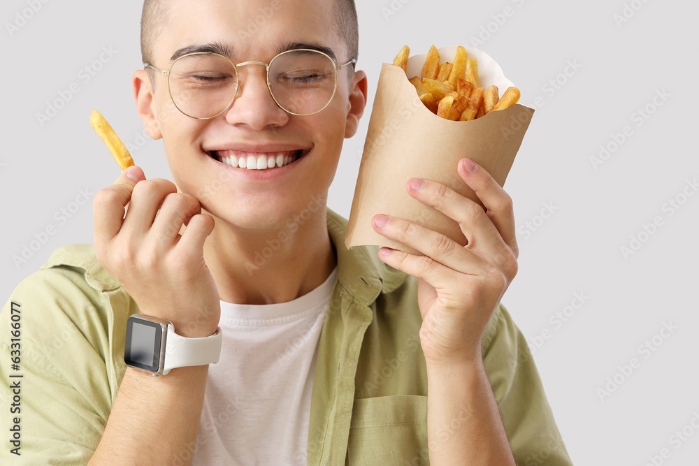 Young man with french fries on light background, closeup