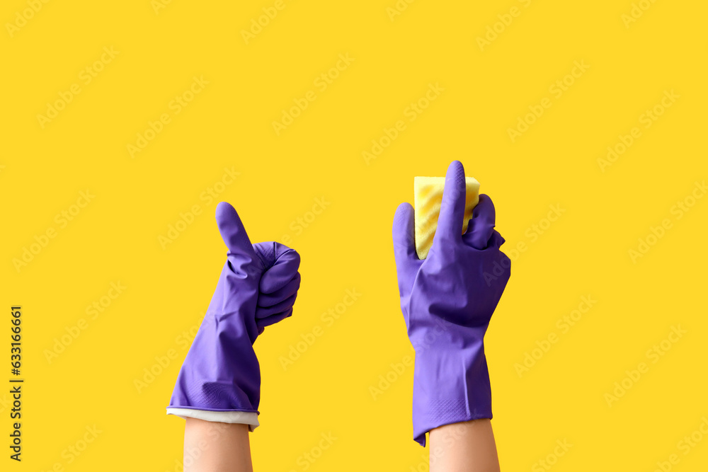 Woman in rubber gloves with cleaning sponge on yellow background