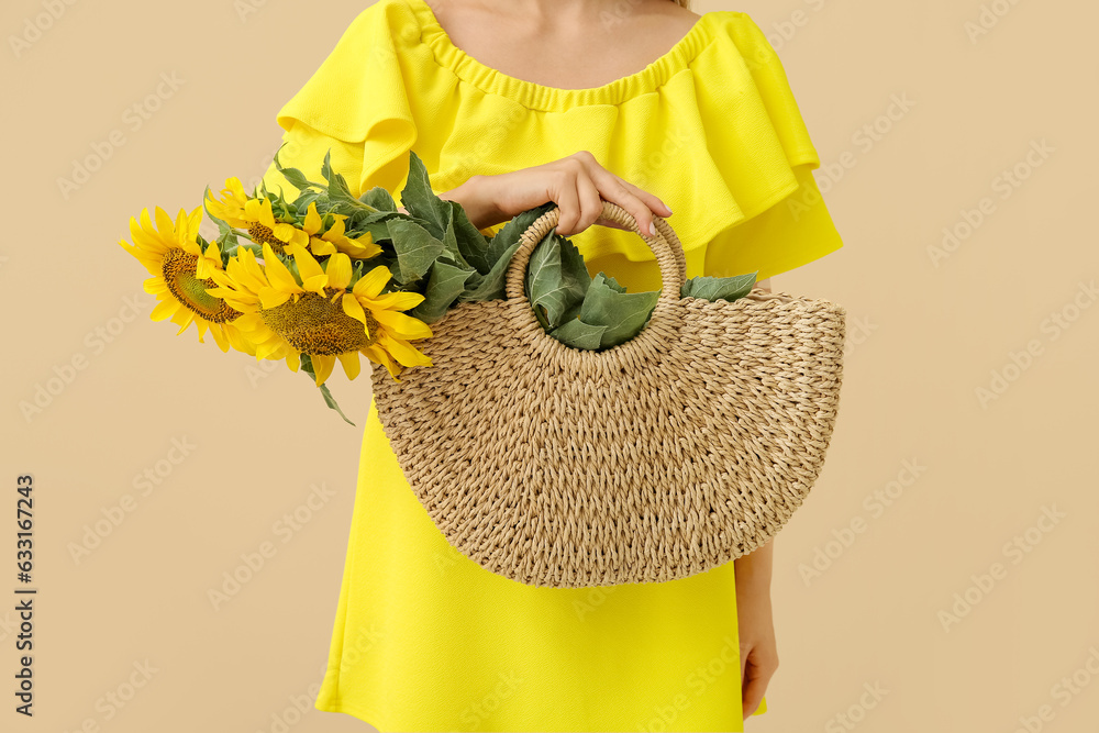 Woman holding wicker bag with beautiful sunflowers on beige background