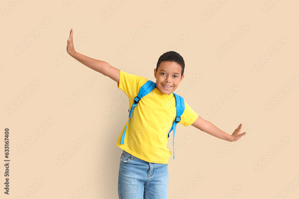 Little African-American boy with school backpack on beige background