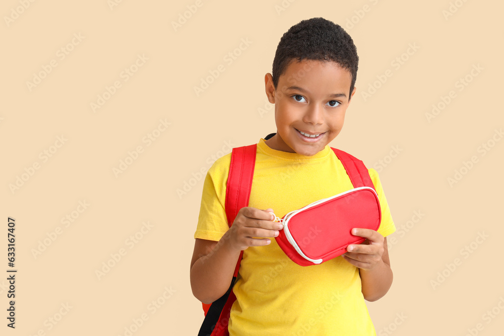 Little African-American boy with school backpack and pencil case on beige background