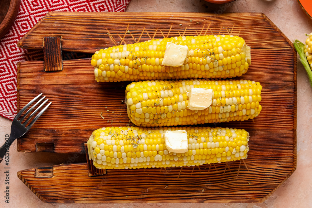 Wooden board of boiled corn cobs with butter on pink background