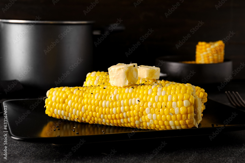 Plate of boiled corn cobs with butter on black background