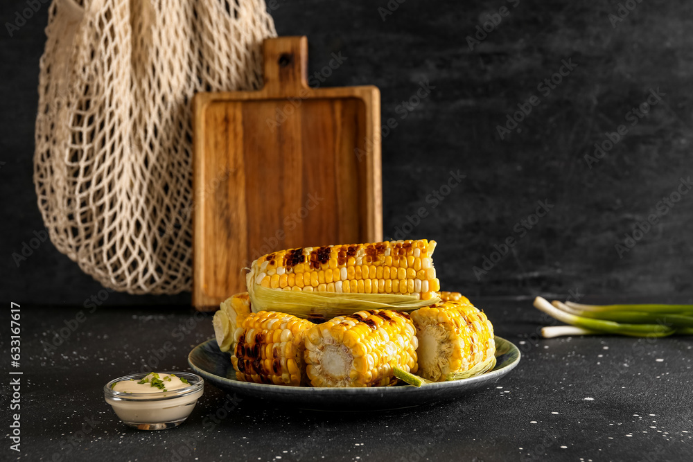 Plate with tasty grilled corn cobs and bowl of sauce on black background