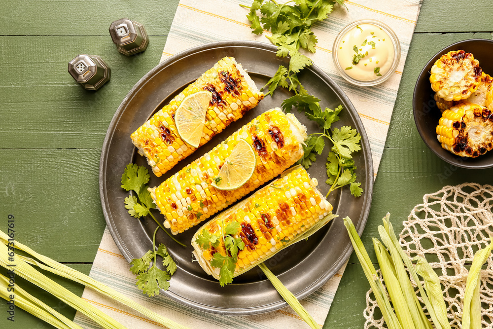 Plate and bowl of tasty grilled corn cobs with parsley on green wooden background