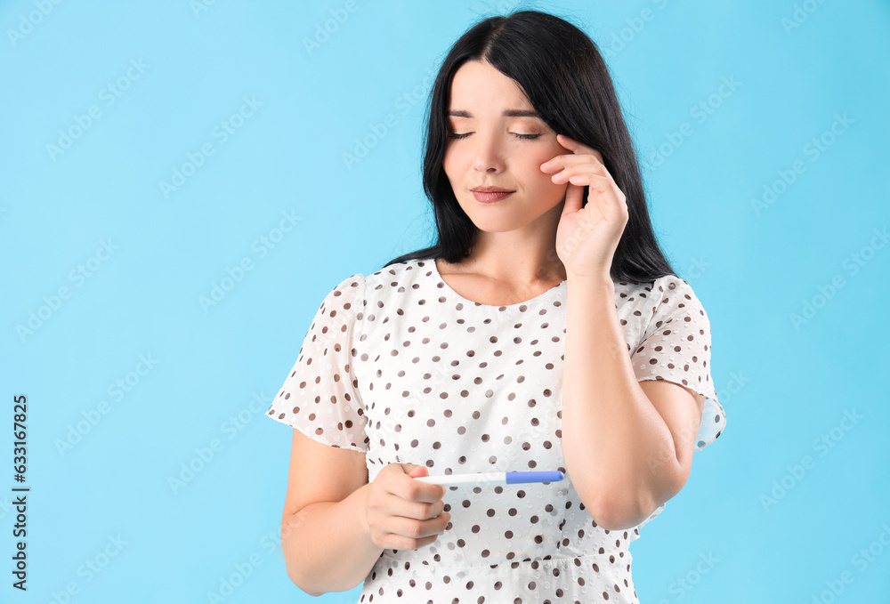 Portrait of worried young woman with pregnancy test on blue background