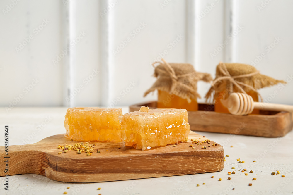 Wooden board with fresh honeycombs and bee pollen on light background