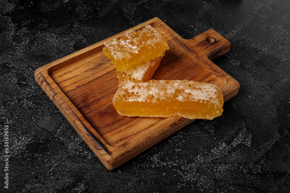 Wooden board with sweet honeycombs on dark background