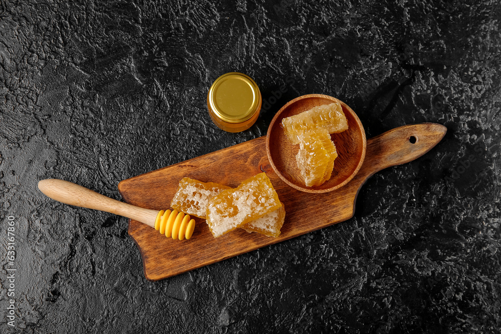 Jar of tasty honey, combs and dipper on dark background