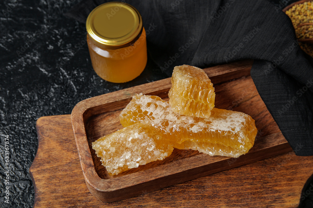 Jar of honey and board with combs on dark background, closeup