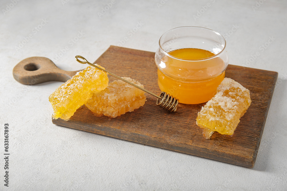 Wooden board with jar of tasty honey and combs on light background